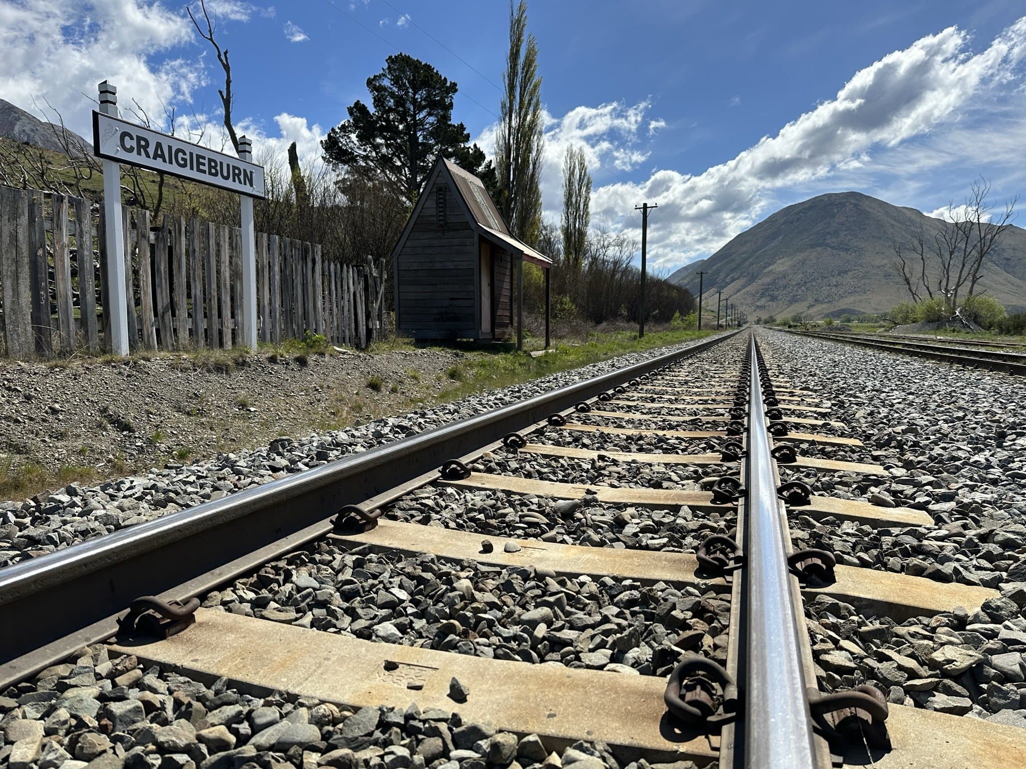 Railway tracks running toward distant mountains past the old Craigieburn station sign and a small wooden shelter
