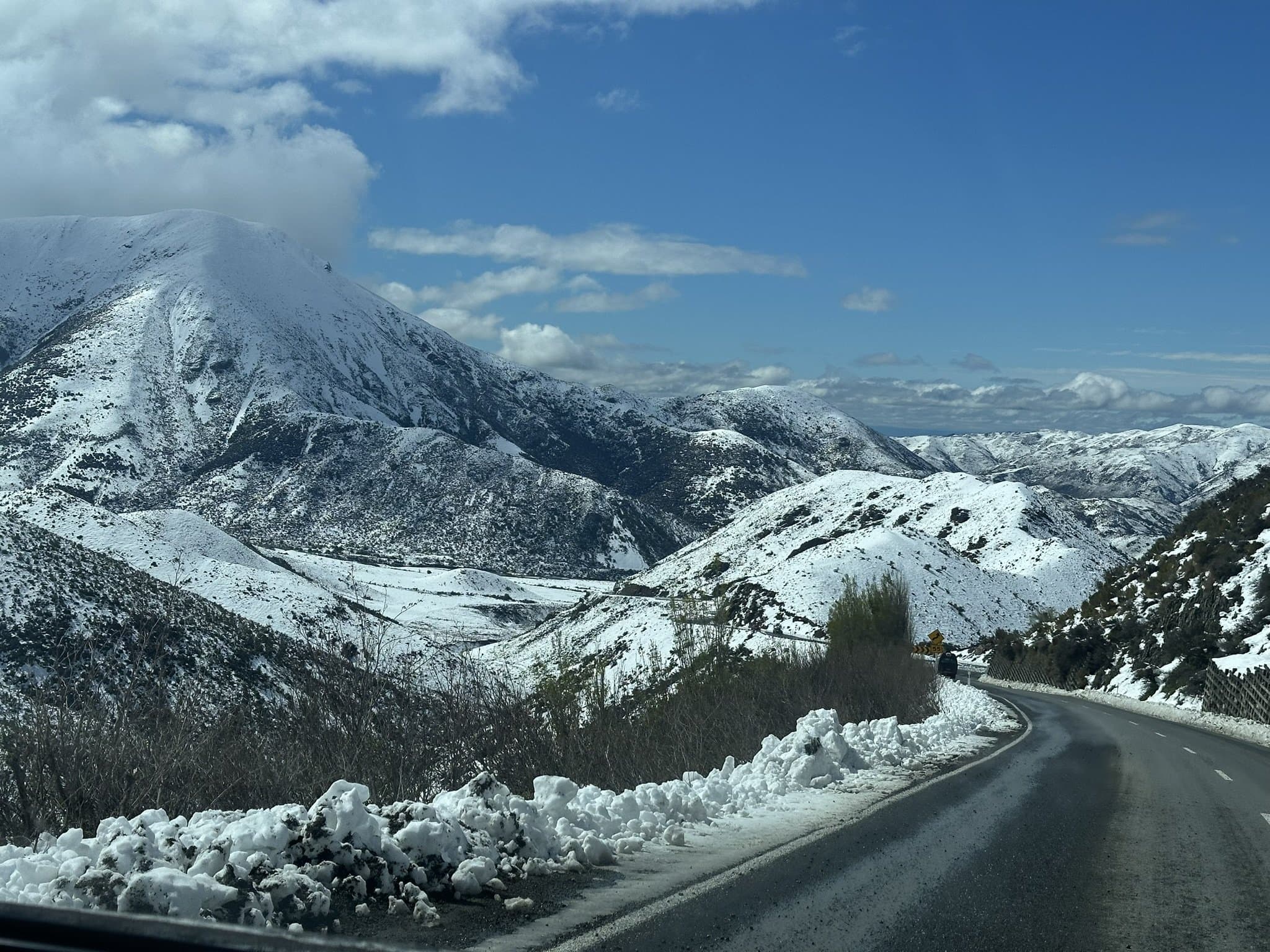 A snow-covered alpine road curving through snowy hills with ploughed snowbanks at the roadside