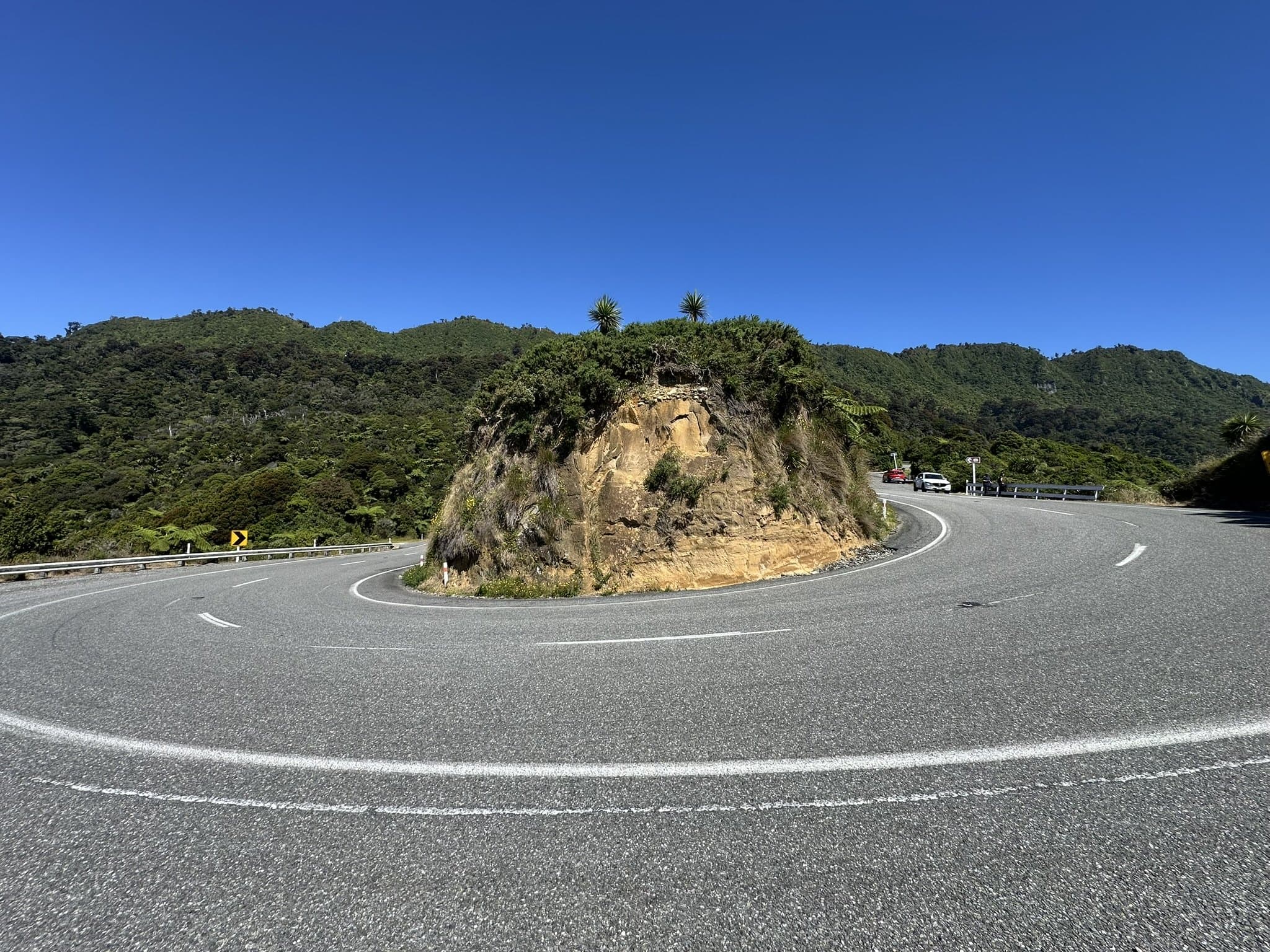 A two-lane highway bending around a steep rocky bluff under a clear blue sky
