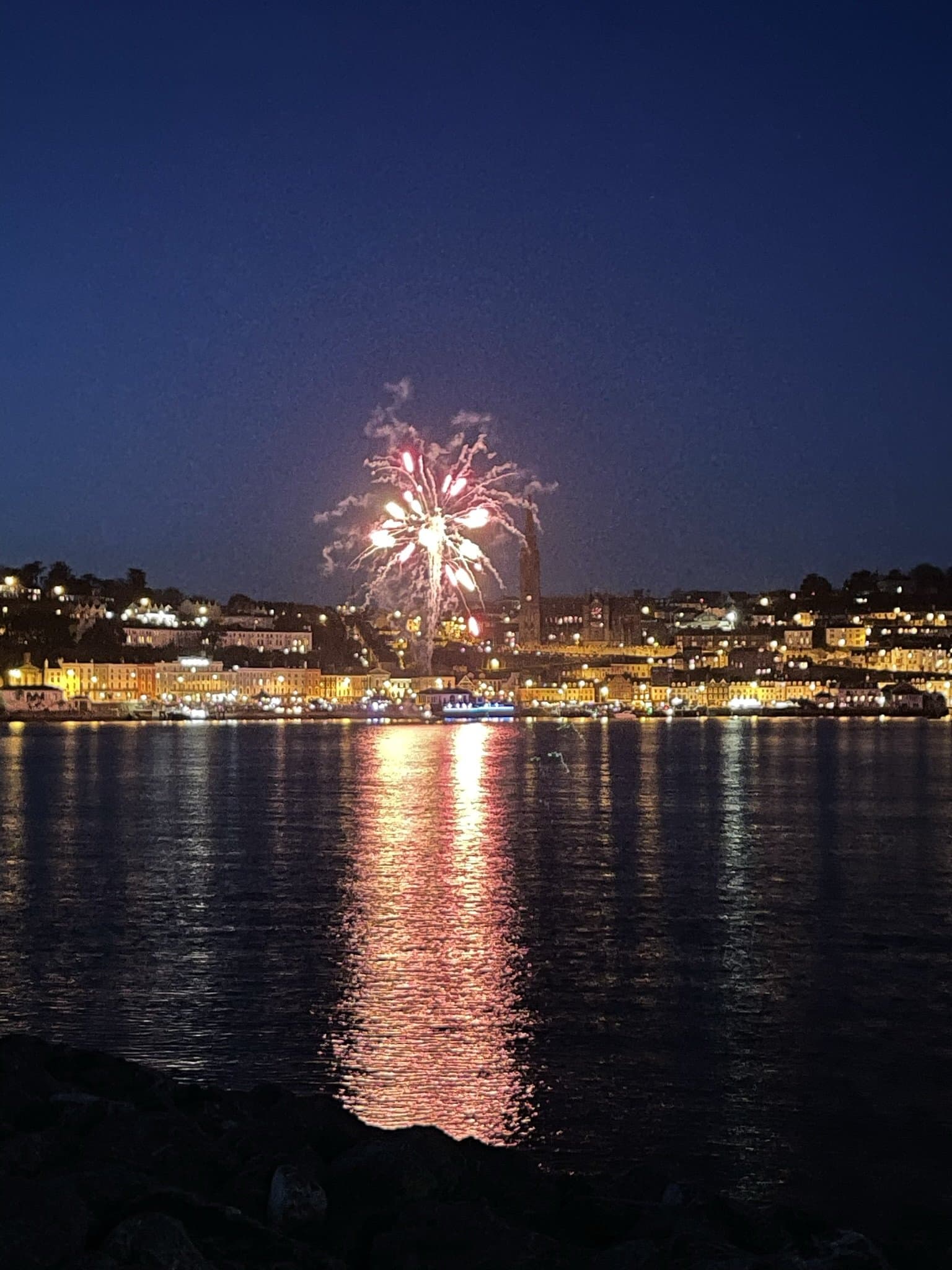 Fireworks bursting in red and gold over a harbour and waterfront town at night