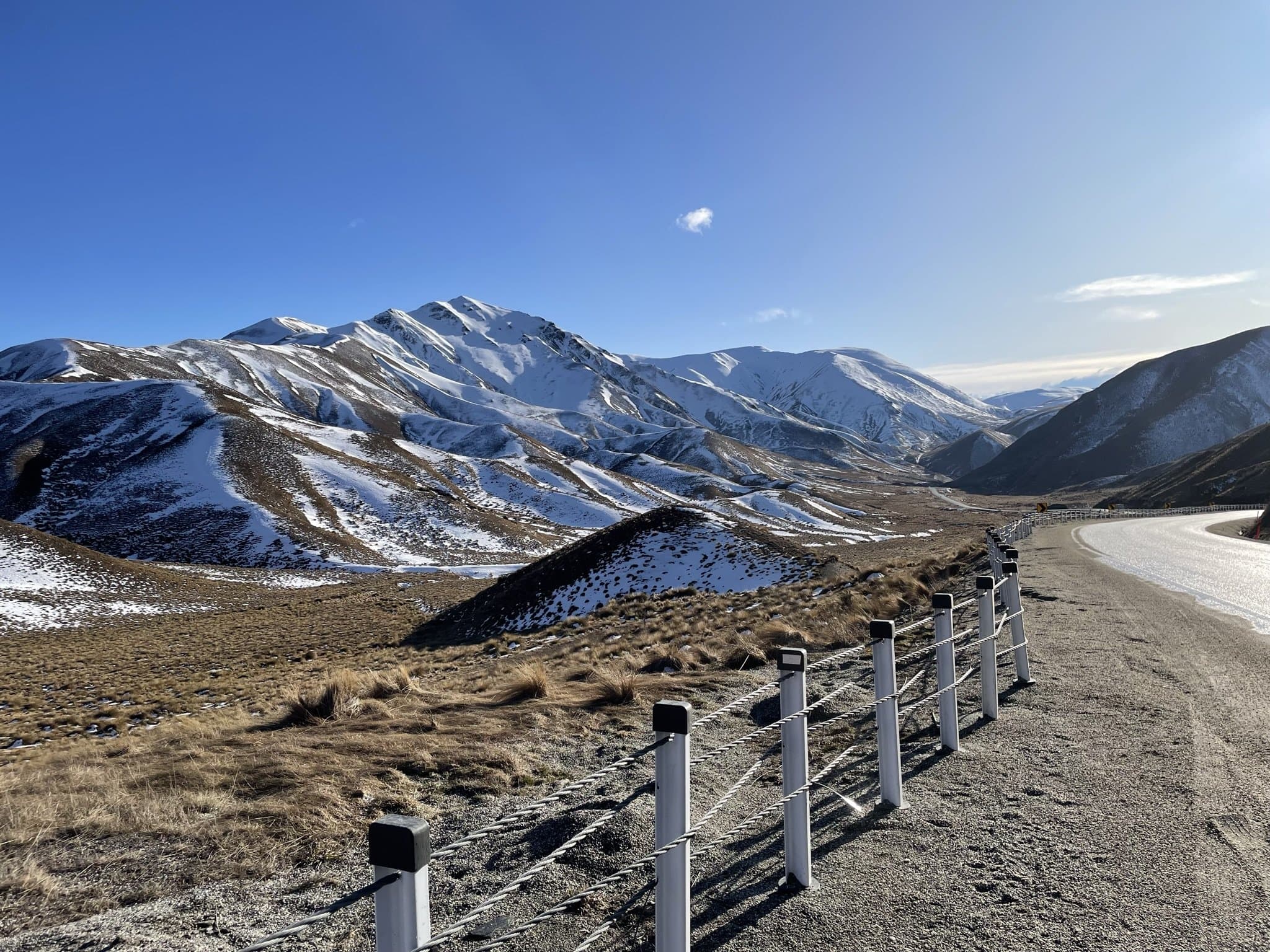 A road curving through golden tussock below the snow-streaked Southern Alps at the Lindis Pass